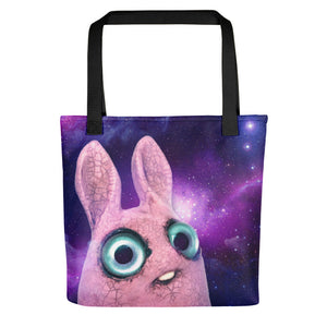 A Pipsqueak Galaxy Tote made from weather-resistant spun polyester featuring a whimsical illustration of a cartoon-like pink creature with large, expressive blue eyes set against a vibrant cosmic starfield background from Bindlewood Shop.