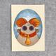 Illustration of a cute, round mouse with big orange ears, a brown nose, and wearing a yellow scarf, all set in an oval frame on a textured gray background.