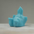 A small, smooth, blue sculpture of a playful animal lying on its back with its legs in the air, crafted by Chris Ryniak. Placed on a wooden surface against a plain grey background, this opaque resin figure features soft contours and minimal detailing.

Product Name: Robin's Egg Blue Bugbite
Brand Name: Chris Ryniak