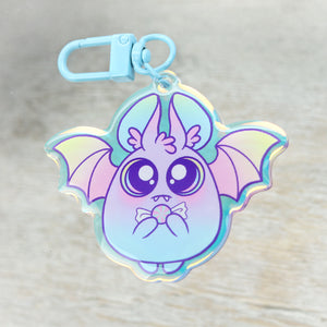A colorful holographic keychain featuring a cute cartoon bat with big eyes and a tiny bow tie, inspired by Amanda Spayd, featuring the "Candy Bat" Rainbow Acrylic Charm from Bindlewood Shop.