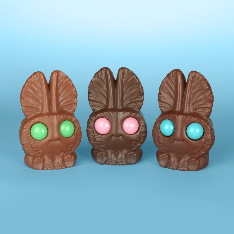 Three Cabbage (Chocolate Assortment) figures from Bindlewood Shop—each with big round candy eyes in green, pink, and blue—are arranged side by side on a blue background, evoking the look of a Chris Ryniak collectible.