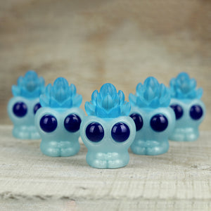 Blue Ice Frost Archie resin figures with large, round eyes and sculpted tops on a wooden surface, aligned in two rows, focus on the front figure. By Chris Ryniak.