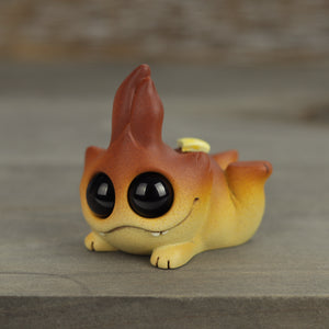 The Handpainted Butterbutt Bugbite by Chris Ryniak is a cute resin figurine with big black eyes, a yellow-orange gradient body, and a flame-shaped tuft on its head, lying on its belly.