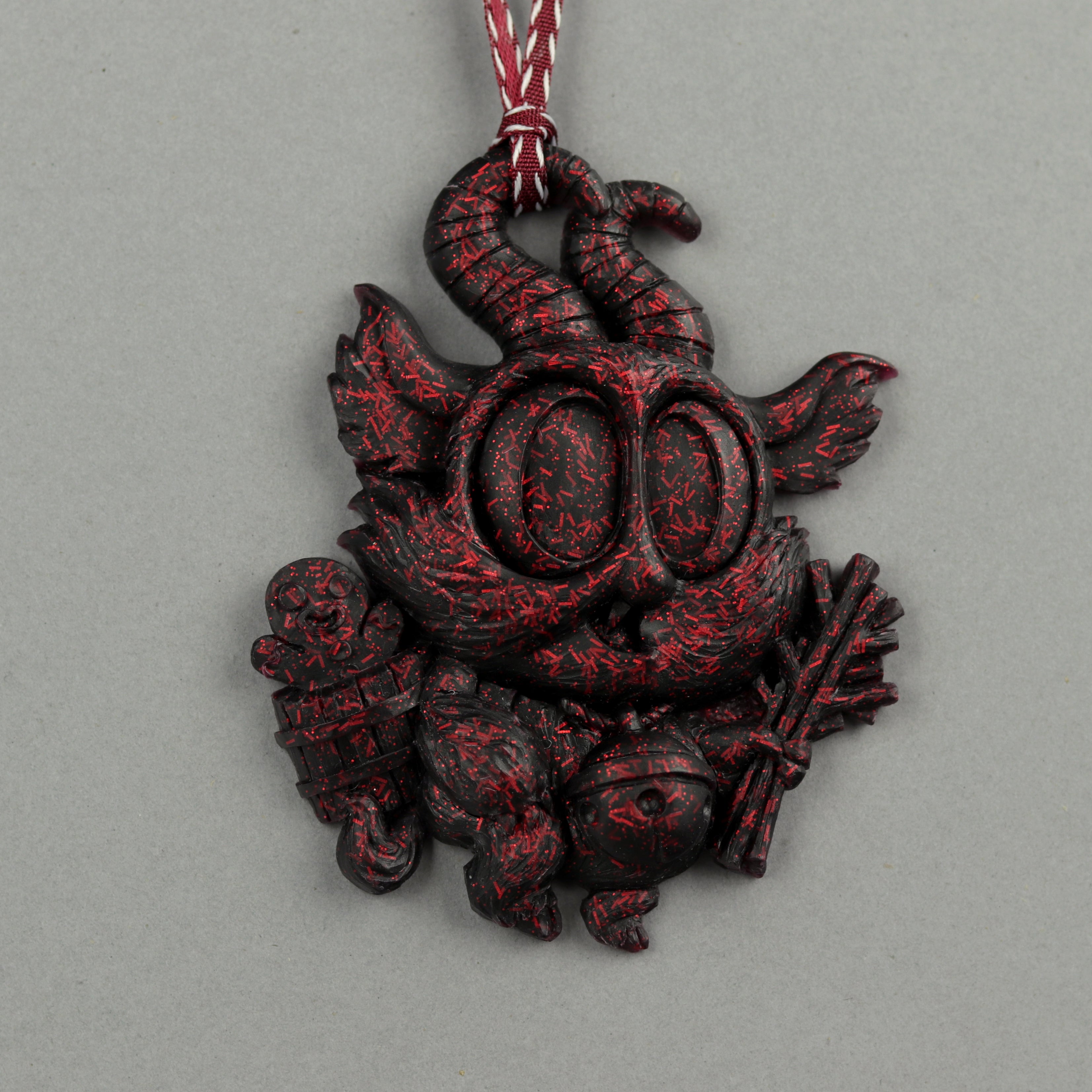 The Bindlewood Shop’s Glitter Krampus Ornaments feature Chris Ryniak’s Lil’ Krampus in sparkly black resin with red speckles, holding sticks and a gingerbread man. It has horns, big eyes, pointy ears, and hangs from a festive red ribbon.