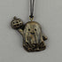 The Bindlewood Shop’s Painted Mini Ornaments feature a bronze pendant inspired by Chris Ryniak—a smiling ghost with a jack-o’-lantern—hanging from a black cord against a plain gray background.