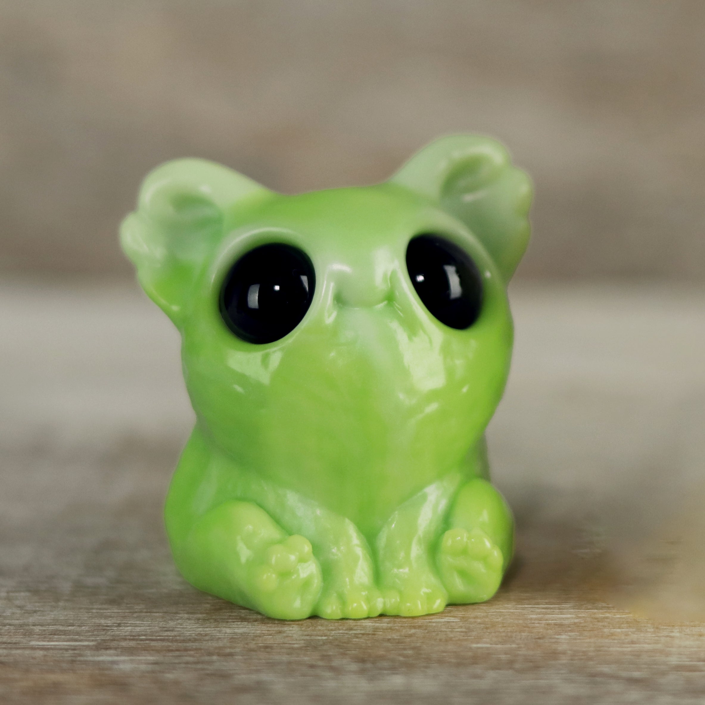 The Key Lime Smidgen by Chris Ryniak is a small, glossy green resin koala figure with oversized black eyes, large ears, and tiny paws, creating a cute and whimsical look.