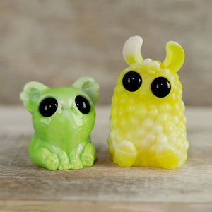 The Bindlewood Shop’s Key Lime Smidgen & Lemon Meringue PomPom Set features two adorable figurines side by side: a green Smidgen with big black eyes and a fuzzy yellow PomPom with upright ears.