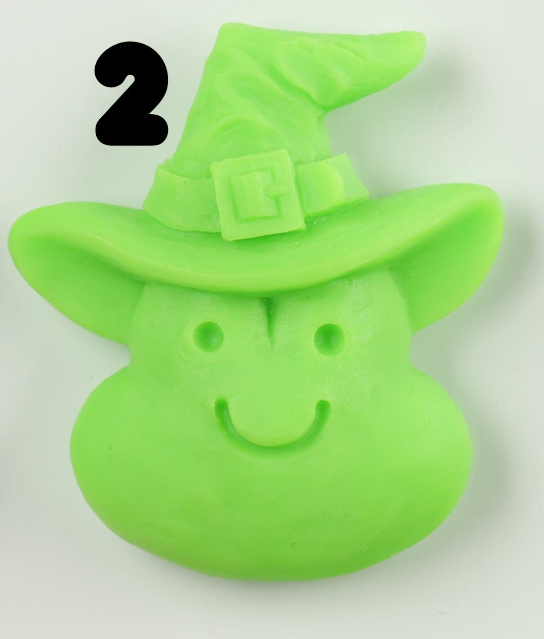 A green, smiling witch face Halloween Magnet from Bindlewood Shop, hand-sculpted and wearing a pointed hat with a buckle. A bold black number 2 appears in the top left corner of the image.