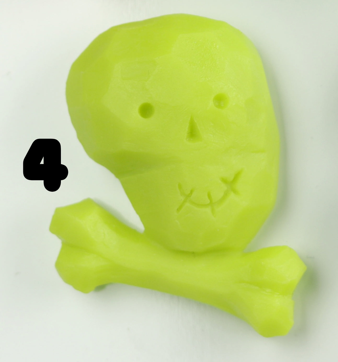 A bold, bright green skull with stitched mouth and round eyes sits on a bone by the number 4. Hand-sculpted details stand out on a white background. Halloween Magnets from Bindlewood Shop are perfect for unique resin decor!.