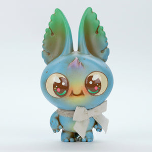 The Blue Kangorumple from Bindlewood Shop is an adorable, small figurine featuring a large head and big, round eyes. Hand-painted in shades of blue and green, it boasts big bunny-like ears with small leaf shapes at their tips. To complete the look, it wears a charming white bow around its neck, and its cheerful facial expression adds to its endearing charm.