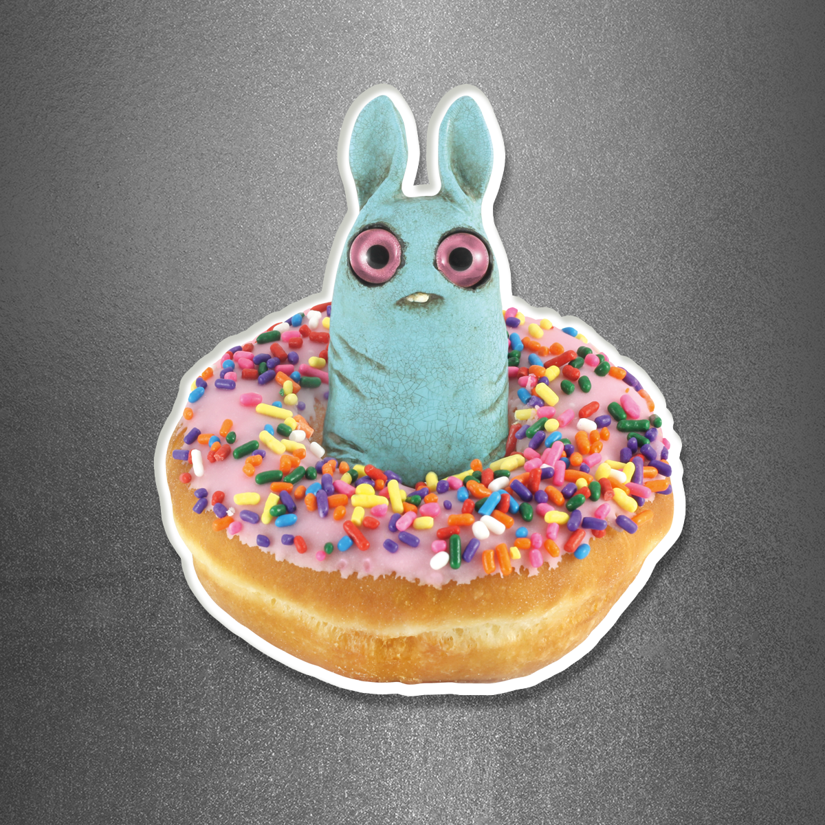 The Donut Pip Magnet by Bindlewood Shop features a pink frosted donut with colorful sprinkles and a blue, bunny-shaped figure with big pink eyes standing in its center, set against a gray background—perfect as a playful acrylic magnet to brighten up your fridge.