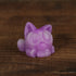 A small, purple Studgy figurine by Chris Ryniak, hand-cast from resin and featuring large round eyes in a cat shape, sits on a wooden surface.