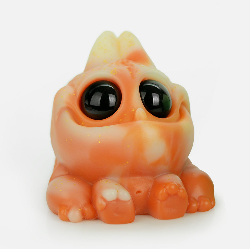 The Chris Ryniak Thai Tea Tank is a small, chonky, orange and cream-colored creature with big glossy black eyes, chubby cheeks, and tiny paws, posed cutely on a white background—just like a signature Ryniak resin figure.