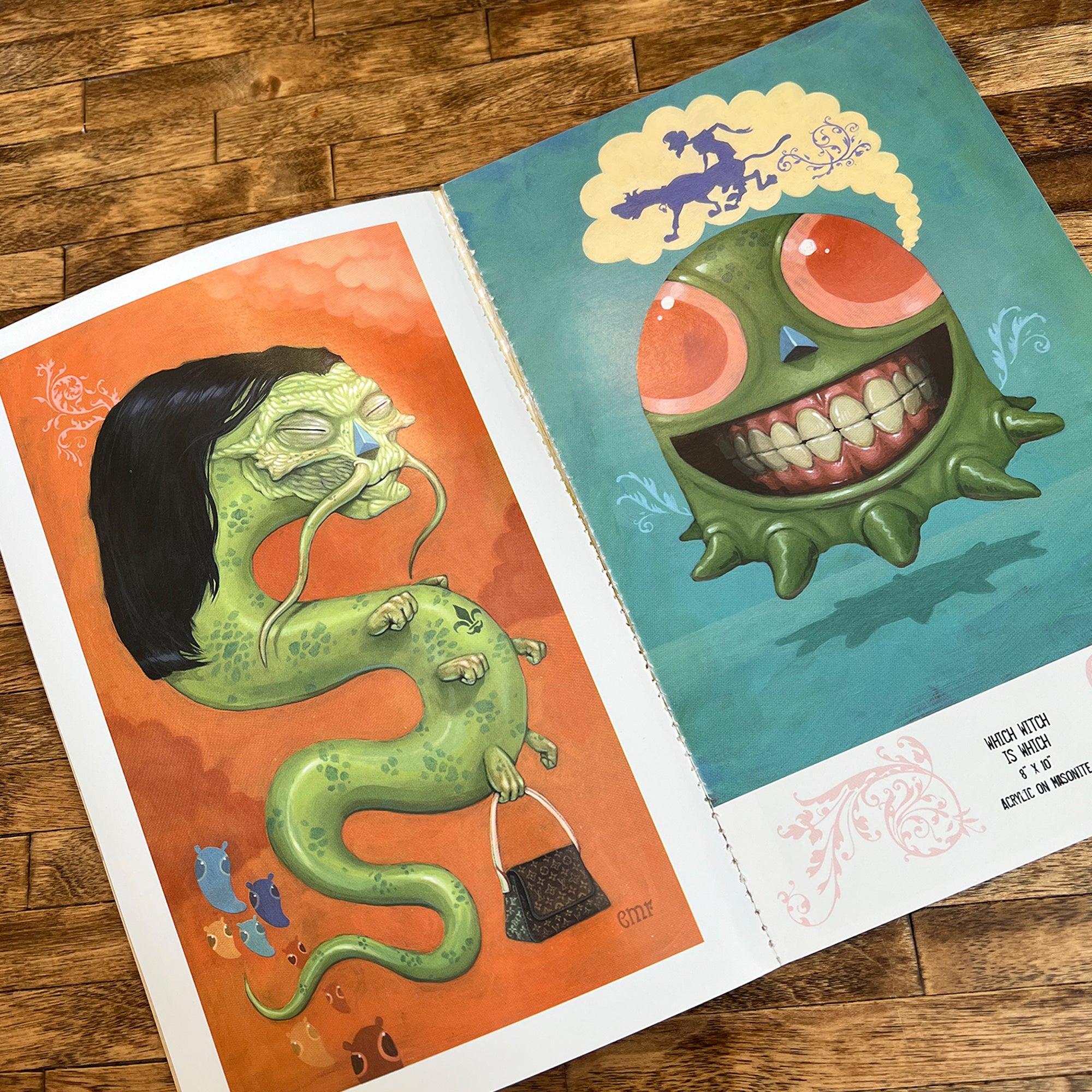 An open copy of "Weird Things are Happening in the Future" by Bindlewood Shop lies on a wooden table, displaying vibrant art of a green snake-like figure with a human mask and a grinning green creature with red eyes and yellow hair.