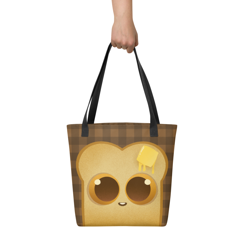 A hand holds the Toast-Bag Tote by Bindlewood Shop, a durable bag with black straps featuring a cute cartoon toast with big eyes and melting butter on its head, set on a brown checkered background.