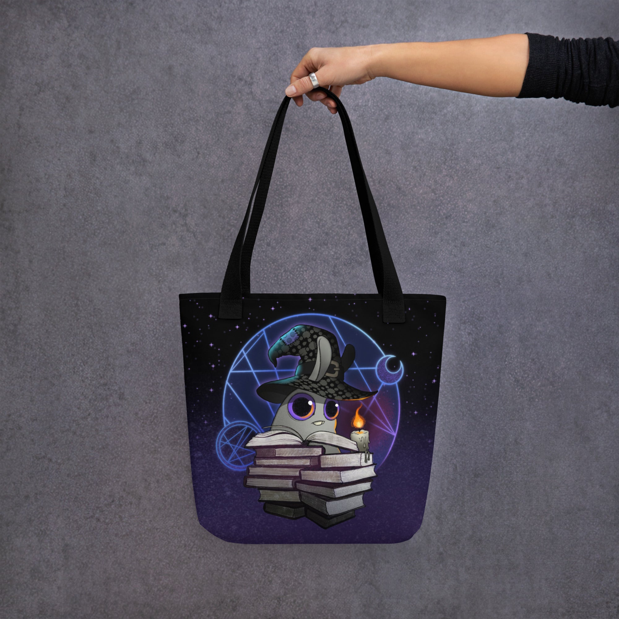 A hand holds the Mystical Witchbunny Tote from Bindlewood Shop, featuring a cute witchbunny in a wizard hat among magical symbols—perfect for Amanda Louise Spayd fans.