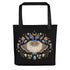 The Bindlewood Shop's Moth Magic Tote is a sturdy, weather-resistant bag featuring a vibrant symmetrical moth with large eyes, surrounded by mushrooms, leaves, crystals, acorns, and a crescent moon.
