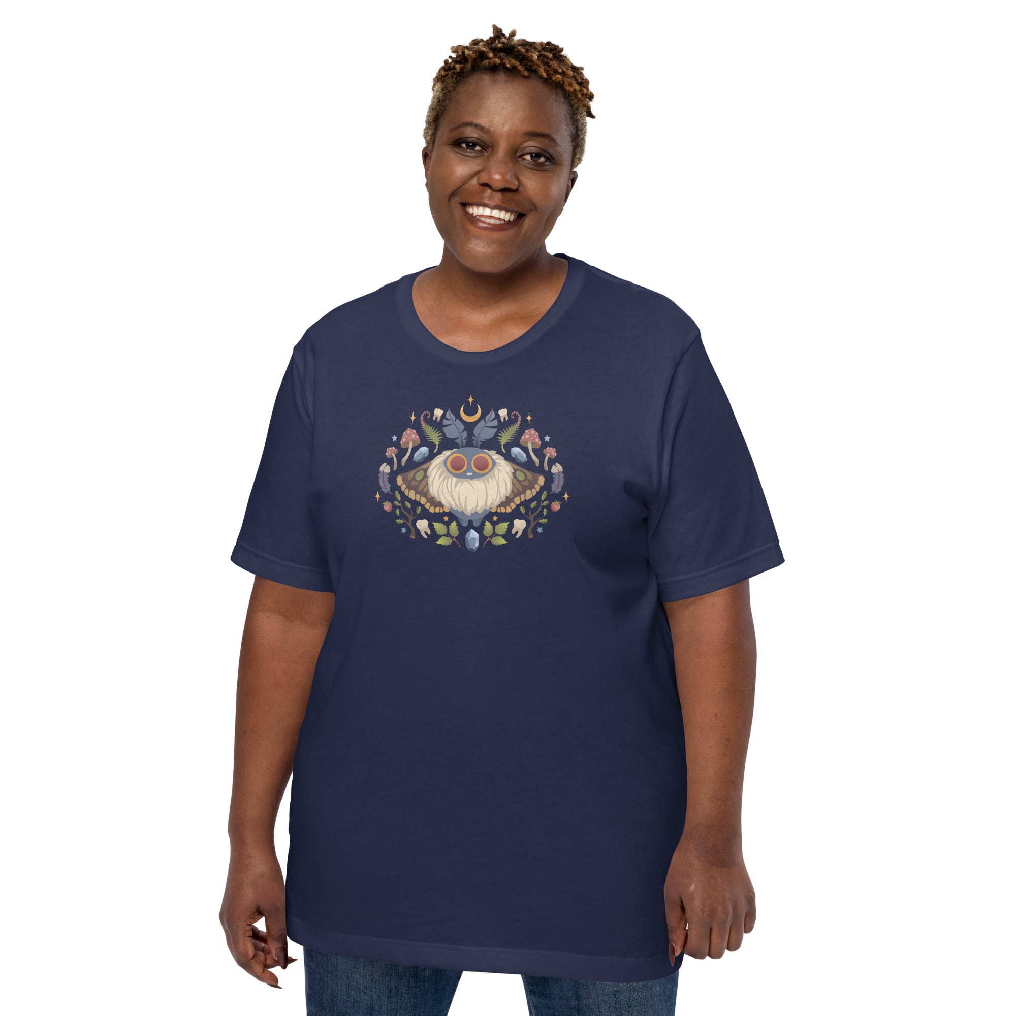 A smiling person wears the Bindlewood Shop's Moth Magic Tee—a navy blue, unisex shirt with a detailed moth, vibrant mushrooms, and leaves. The plain white background highlights this enchanting forest design.