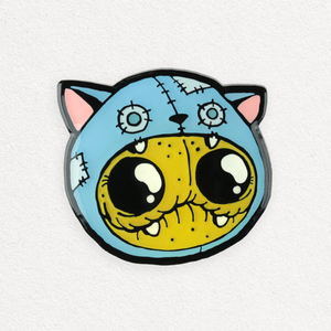 A quirky enamel pin featuring a cartoon-style, stitched-up zombie cat with large, expressive eyes and a vibrant yellow face against a light background, called the Catstume Pin from Bindlewood Shop.