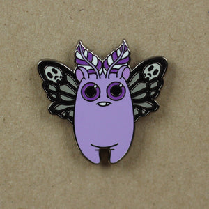 A whimsical hard enamel pin featuring a purple character with skull-decorated wings and playful antenna, inspired by the Death's Head Moth, called the Death's Head Mothbunny Pin from Bindlewood Shop.