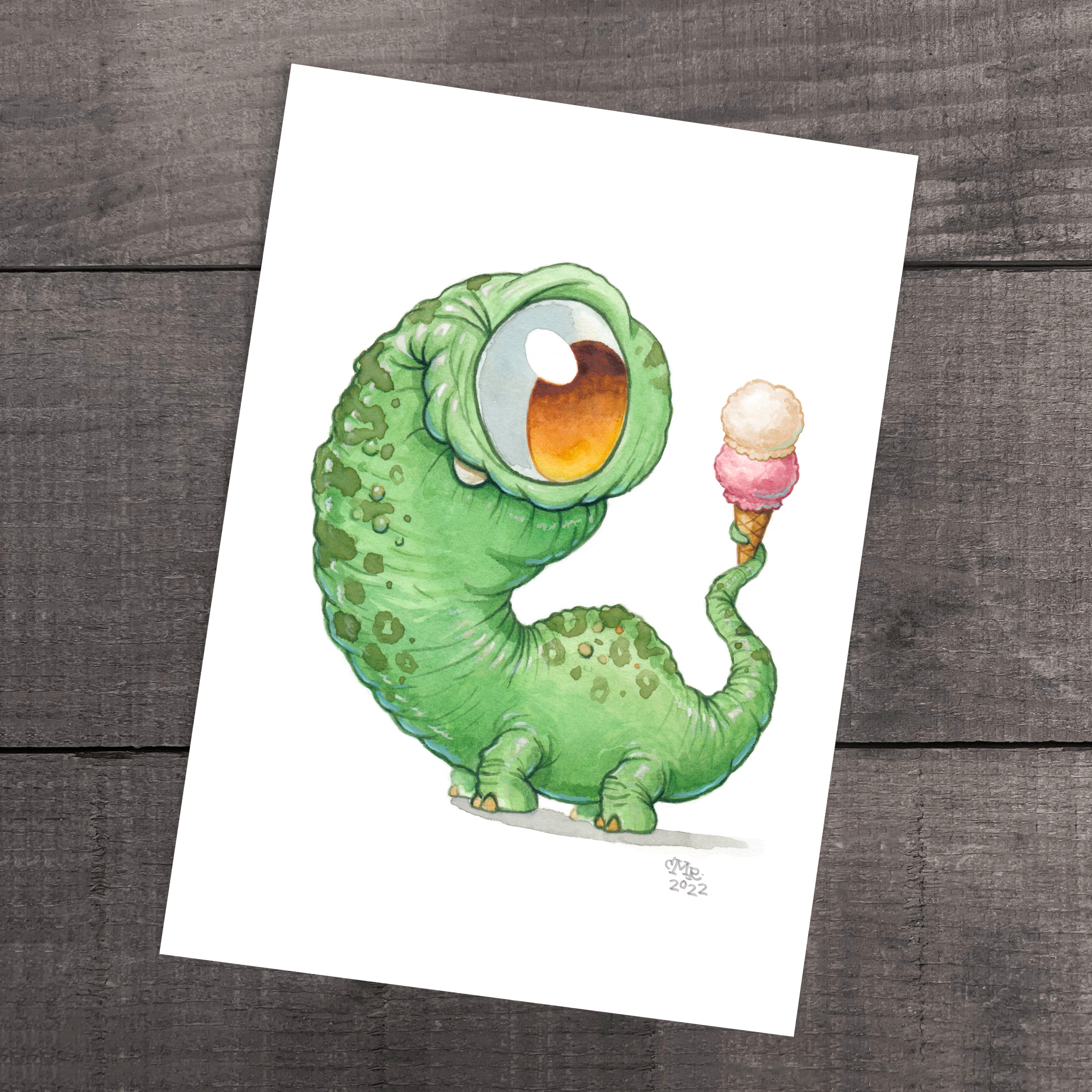 The "Dino Scoops" print by Chris Ryniak showcases a whimsical, green cartoon-like creature with an oversized single eye and textured skin, holding a two-scoop ice cream cone with its tail. This fine art print is presented against a wooden background and is available on archival paper.