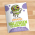 The cover of the "Morning Scribbles Coloring Book - Halloween Edition" from Bindlewood Shop lies on a wooden surface, featuring a cute cartoon mummy with large, expressive eyes, bat wings, and purple clouds. An exclusive pre-order postcard is included, along with fifty more pages of spooky monster doodles.