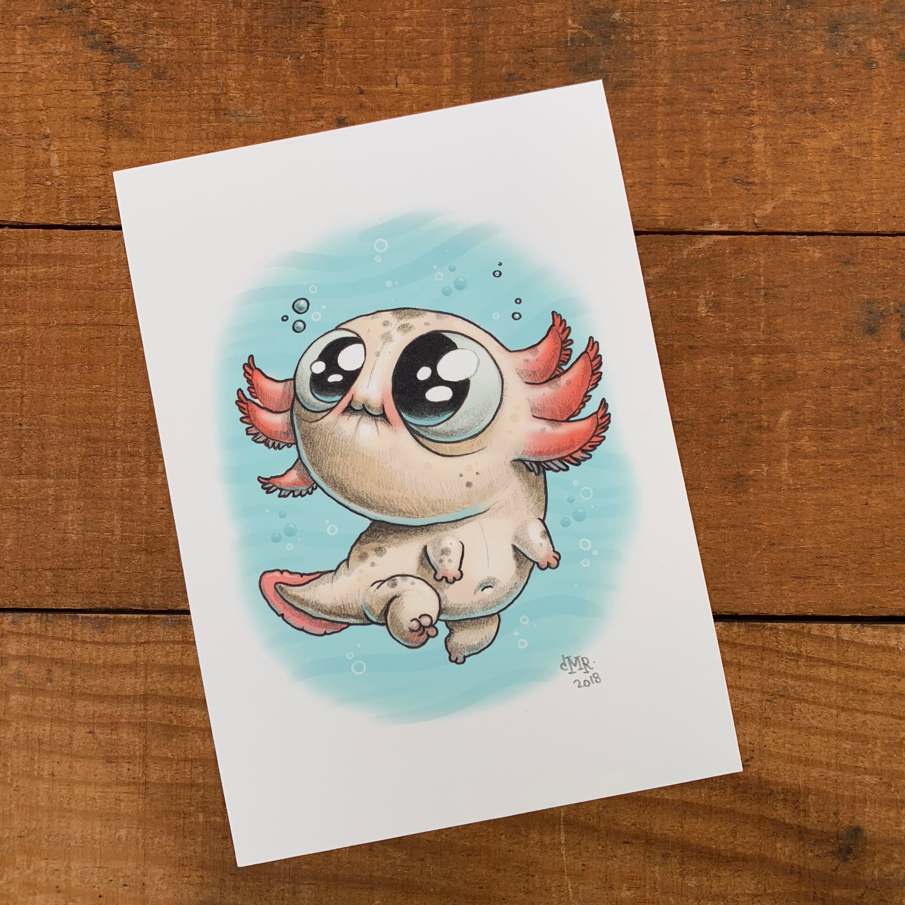 A drawing of a cartoon character from Bindlewood on a wood surface featuring the "Axolotl" print by Chris Ryniak.