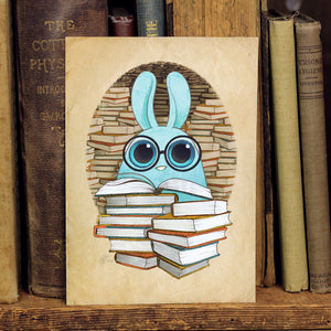 A whimsical illustration of a blue bunny with glasses peeking out from behind a stack of books, nestled within a cozy Bindlewood library setting featuring the Amanda L Spayd "So Many Books" Print.