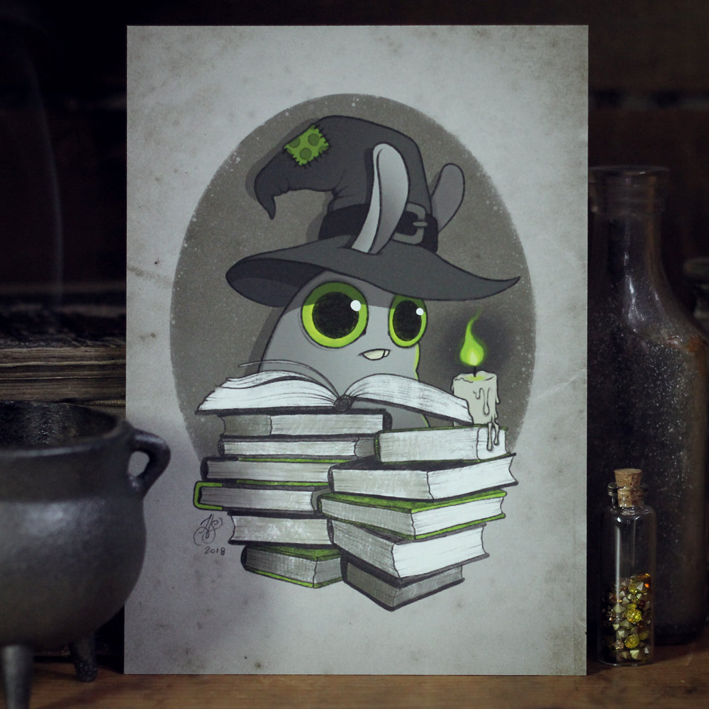 A whimsical artwork titled "Witchbunny" by Amanda L Spayd features a cartoon slug adorned with a wizard hat, ensconced between towers of books. With its large green eyes, it clutches a glowing candle that illuminates an enigmatic background brimming with potion bottles and a cauldron. This enchanting scene has been rendered as a fine art print on archival paper.