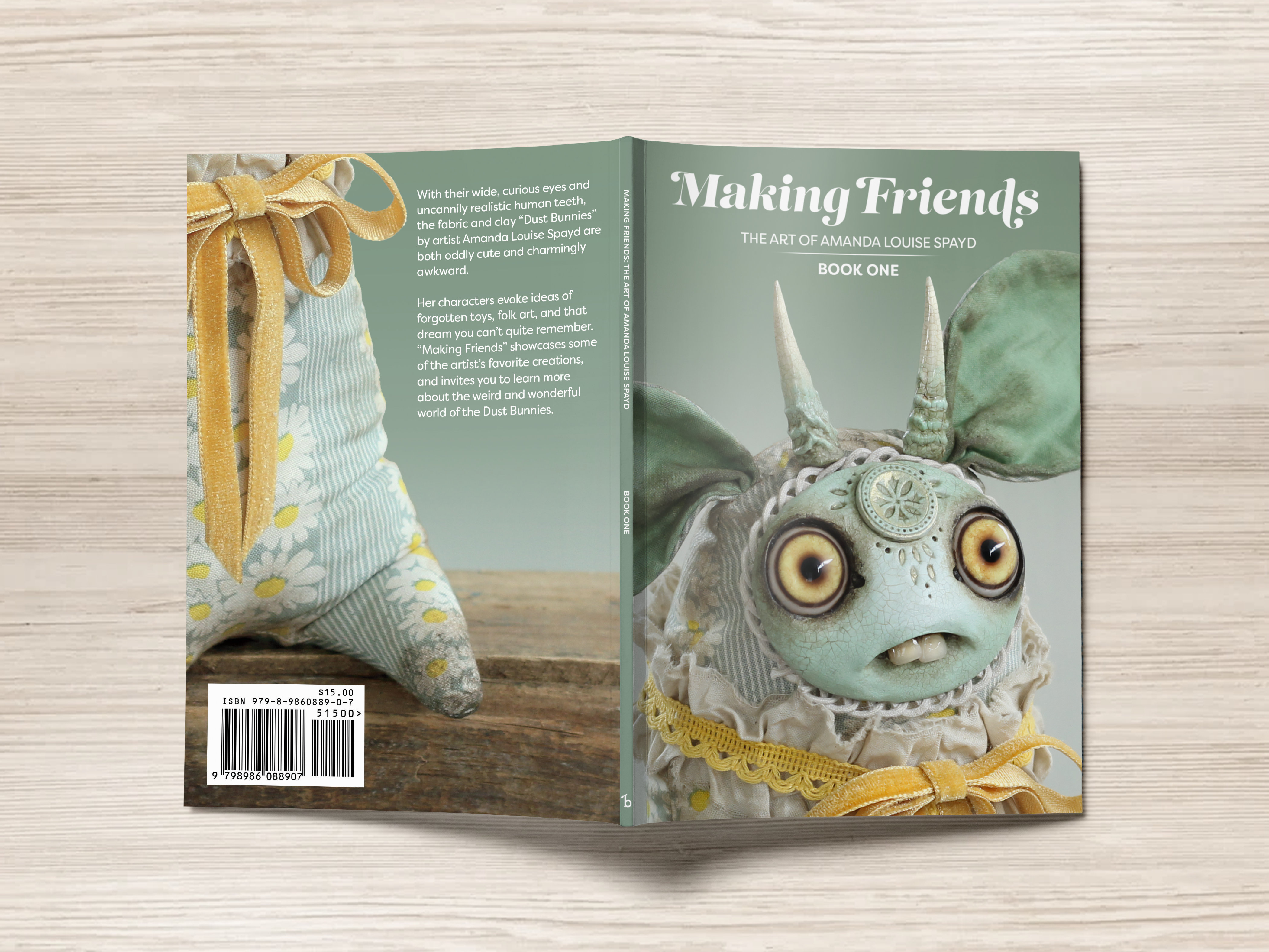 A softcover book from Bindlewood Shop, titled "Making Friends," is placed on a wooden surface. Its cover features a whimsical creature with large eyes and long ears, dressed in lace and a bow. The back of the book highlights a plush doll made from floral fabric, encapsulating the charm of this inaugural volume.