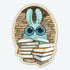 The So Many Books Sticker from Bindlewood Shop features a cute blue Dust Bunny with big round glasses surrounded by stacks of books—an adorable vinyl sticker perfect for book lovers.