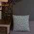 A Bindlewood Shop Twilight Sprite Throw Pillow with a floral pattern rests on a neatly made bed with a gray quilt. The headboard of the bed is upholstered with gray fabric. A wooden nightstand with a lamp, featuring nature-themed wallpaper in the background, complements the cottagecore interior design.