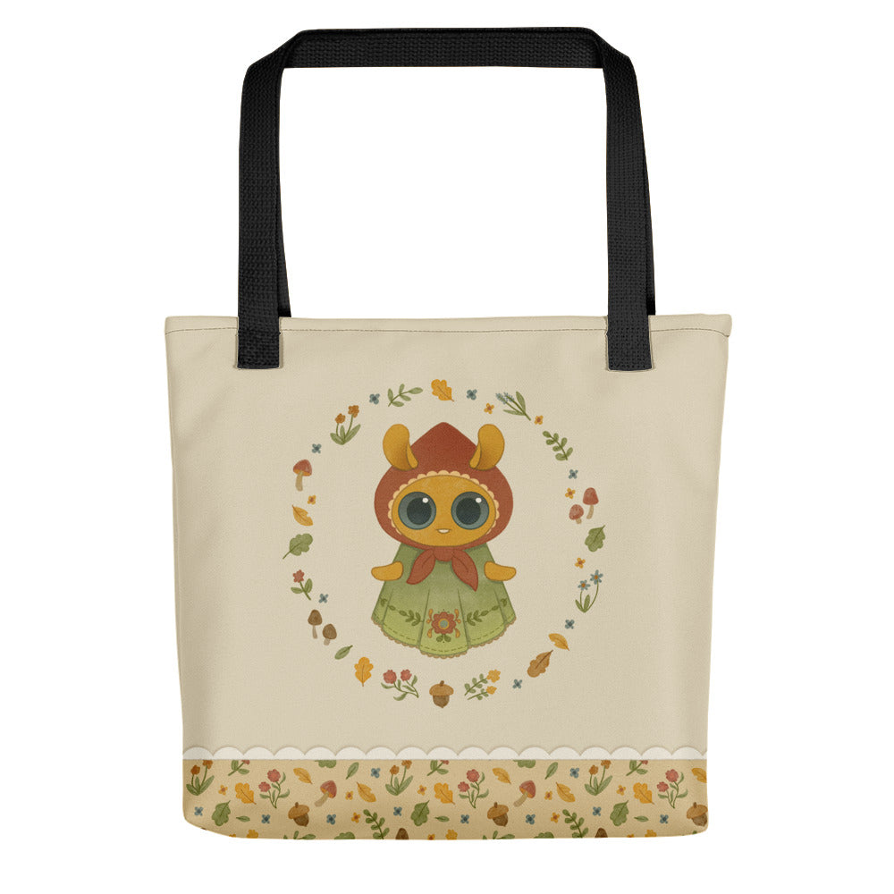 Introducing the Garden Sprite Tote by Bindlewood Shop: a spacious cream-colored bag with black handles. It features a whimsical illustration of an animal-like character with large eyes, clad in a green outfit with a flower headpiece. The design is accentuated by a circular border of flowers and leaves, complemented by a floral pattern at the bottom and the signature Bindlewood logo in the corner.