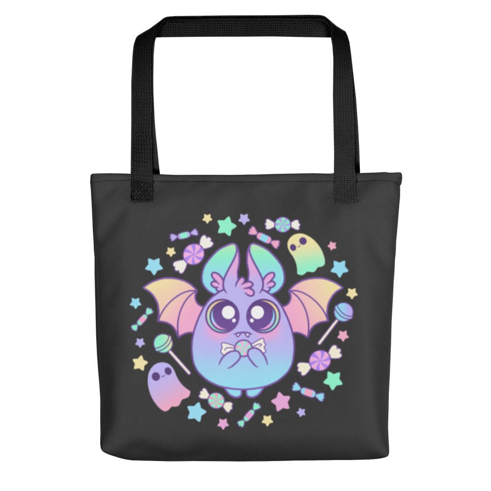 Introducing the Pastel Candy Bat Tote by Bindlewood Shop: a spacious, sturdy black tote bag adorned with a colorful and adorable illustration of a round, pastel bat with large eyes and tiny wings. Made from 100% spun polyester fabric, this whimsical design features the bat surrounded by candies, stars, and ghosts in delightful pastel shades.