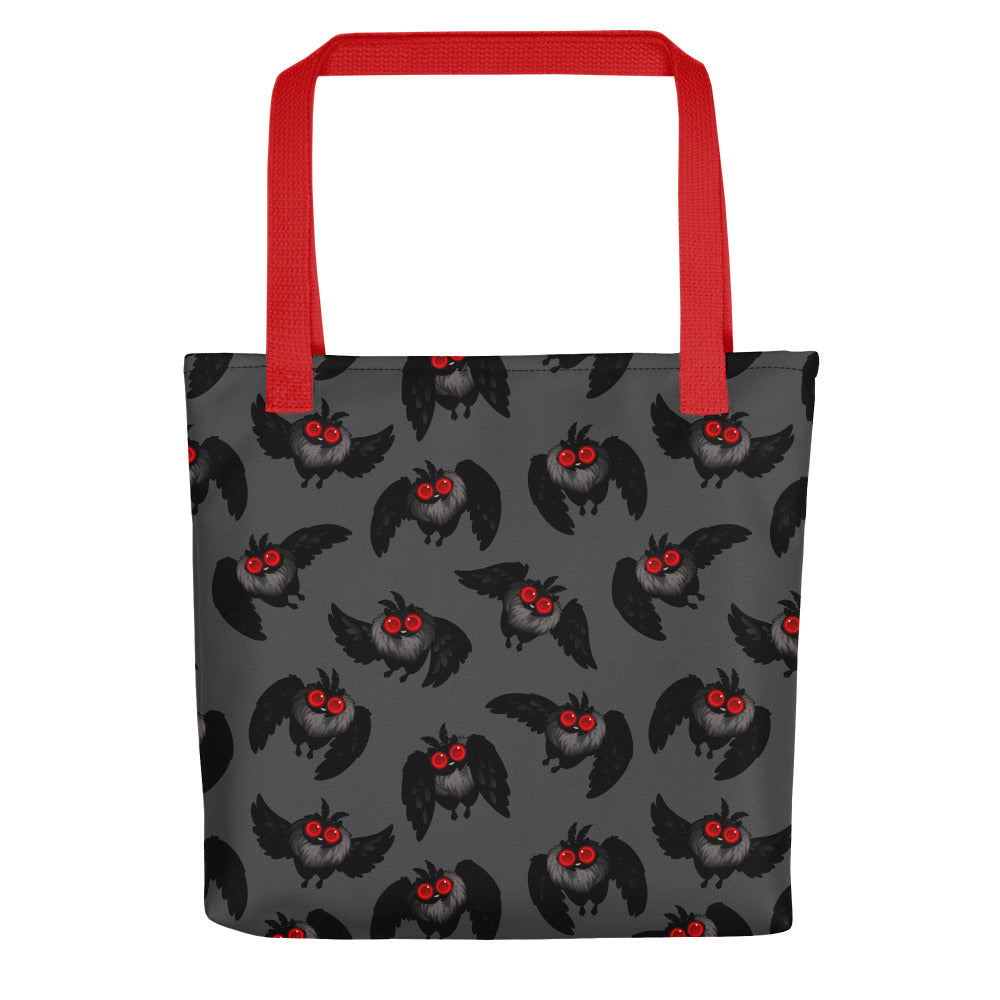 A dark gray tote bag made of durable fabric features a pattern of black cartoon owls with red eyes and beaks. The Mothman Cryptid Tote by Bindlewood Shop, ideal for cryptid-hunting paraphanalia or as a quirky Mothman tote bag, has bright red handles that create a striking contrast with the dark background and design.