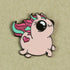 An enamel pin of a cute, chubby unicorn with a pink body, large black eyes, a tiny horn, and a multicolored mane and tail. It has a heart shape on its side and is set against a beige background. This Sparkle Pony Magic Pin from Bindlewood Shop brings an extra touch of whimsy to your collection.