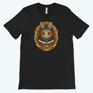 A black "The Maker" Tee featuring a graphic print of a whimsical creature from Thimblestump Hollow, with large eyes, sharp teeth, bunny-like ears, and a decorative mane, tied with a Bindlewood Shop.