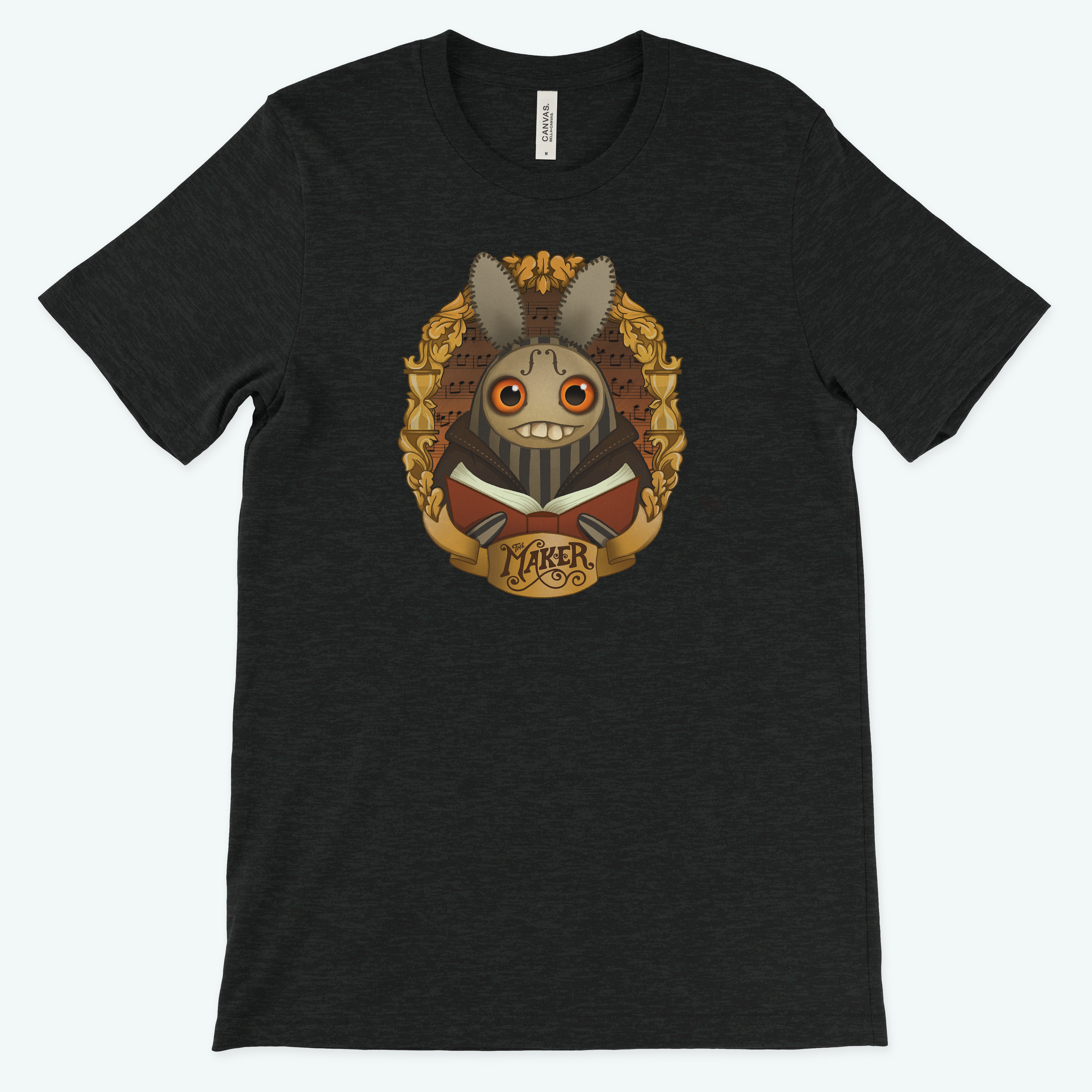 The Maker" Tee by Bindlewood Shop showcases a charcoal gray, gender-neutral design with Amanda Louise Spayd’s art: a stylized rabbit with large eyes and a wide grin within an ornate golden frame. A banner below reads "MAKER," enhancing its artistic appeal.