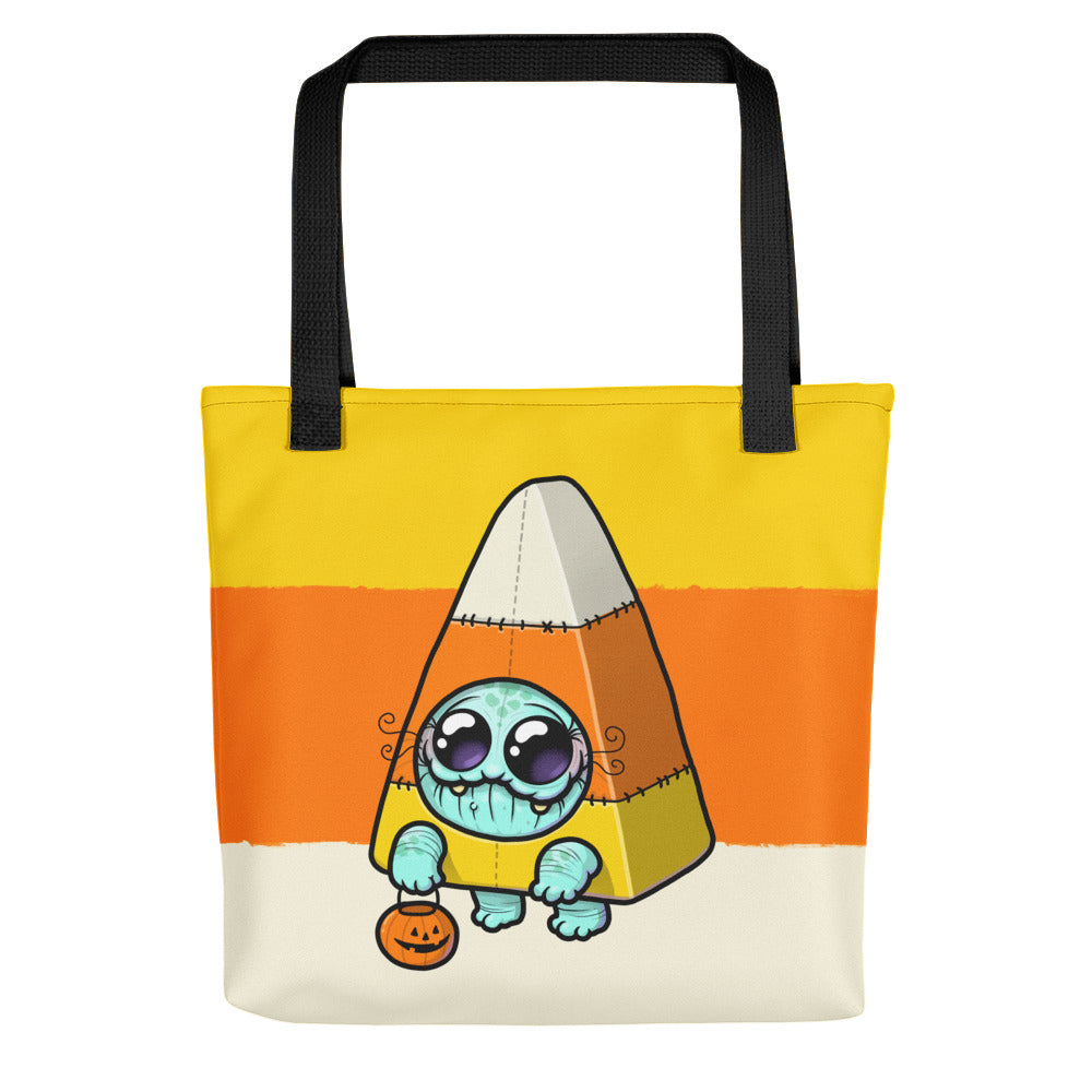 The Candy Corn Tote Bag by Bindlewood Shop features a cute blue big-eyed creature in a candy corn costume with a pumpkin basket, black handles, and a yellow, orange, and cream weather-resistant design—perfect for spooky adventures.