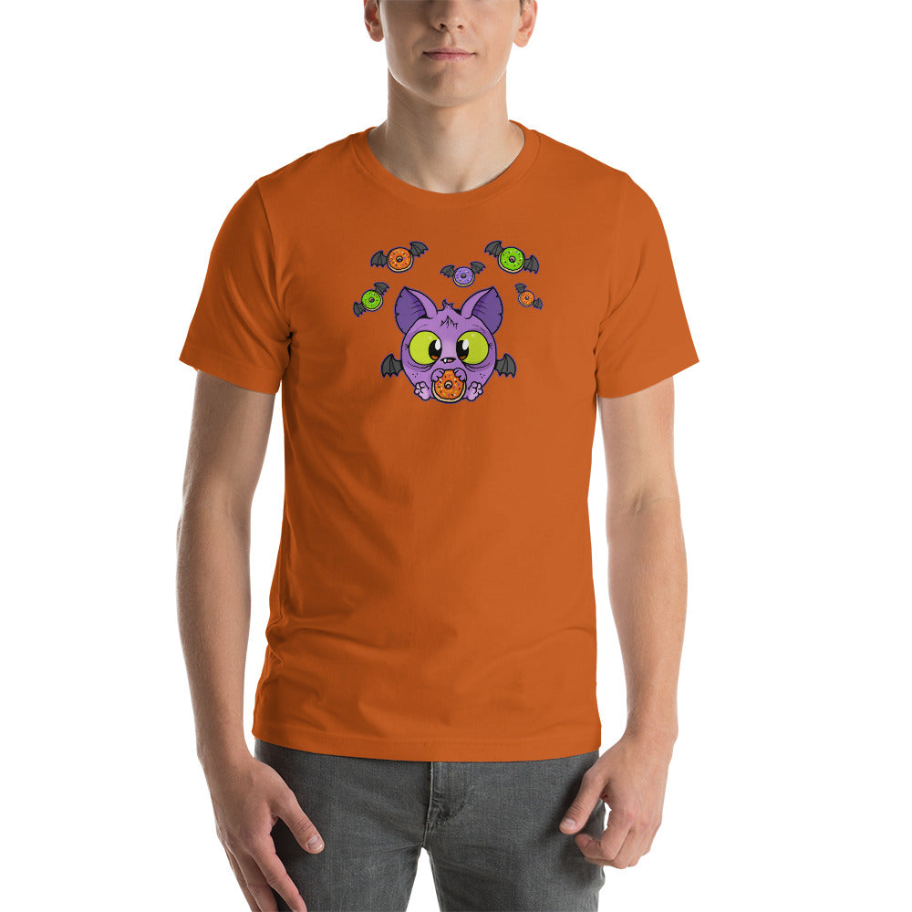 A person wearing the soft and lightweight Donut Bat Tee from Bindlewood Shop, which features a cartoon design of a purple bat with large eyes surrounded by colorful candies on an orange background, stands against a plain white backdrop. Crafted for extra comfort, the t-shirt is made from combed and ring-spun cotton.