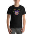 A person is wearing the Donut Bat Tee from Bindlewood Shop, a black t-shirt adorned with a colorful cartoon design on the chest. Made from soft and lightweight combed and ring-spun cotton, the t-shirt features a whimsical purple bat-like creature with wide eyes and extended wings, surrounded by vibrant floating orbs. The person stands against a plain white background.