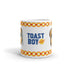 The Toastboy Mug by Bindlewood Shop is a glossy white ceramic mug adorned with "Toast Boy Enriched!" printed in vibrant blue and red text, flanked by charming cartoon images of toast slices. The top and bottom edges feature a delightful checkered pattern in red, yellow, and white. For added convenience, this mug is both dishwasher and microwave safe.