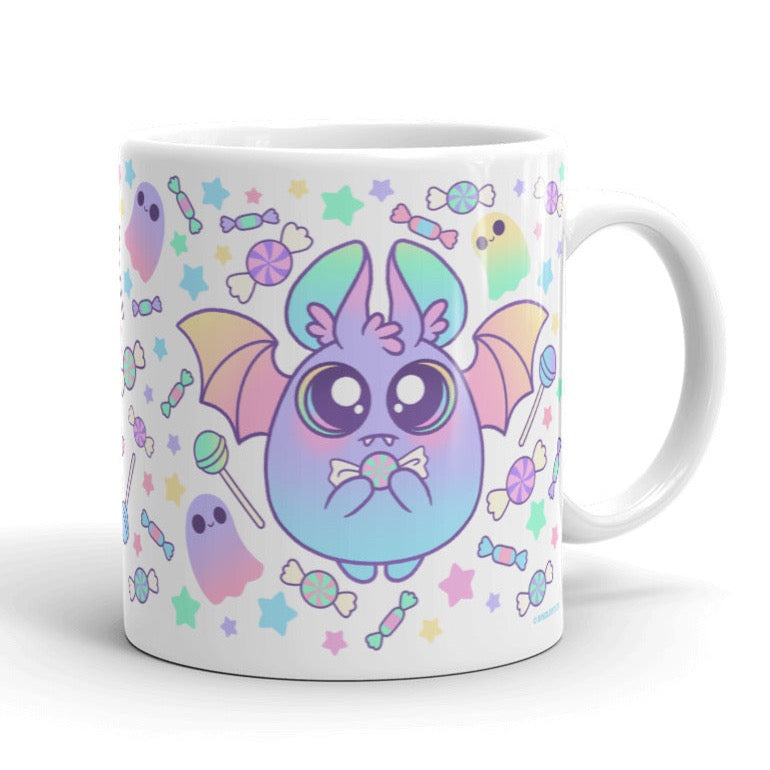 The Pastel Candy Bat Mug from Bindlewood Shop showcases a delightful, round creature with large eyes, bat wings, and holding a bow. The background is beautifully decorated with colorful stars, candies, and small ghost-like figures in soft pastel hues. This whimsical and playful ceramic mug is also dishwasher and microwave safe.