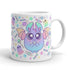 The Pastel Candy Bat Mug from Bindlewood Shop showcases a delightful, round creature with large eyes, bat wings, and holding a bow. The background is beautifully decorated with colorful stars, candies, and small ghost-like figures in soft pastel hues. This whimsical and playful ceramic mug is also dishwasher and microwave safe.