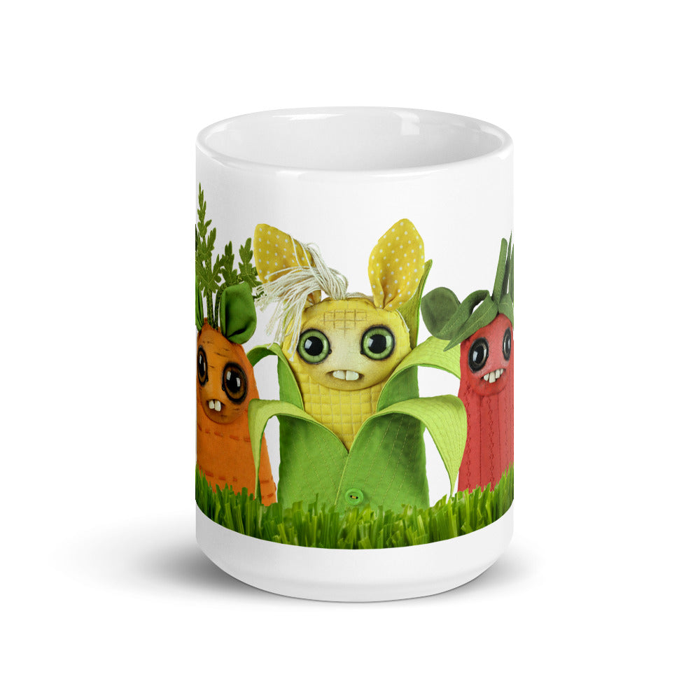 The Farm Market Dust Bunnies Mug from Bindlewood Shop is a white ceramic mug adorned with three colorful, cartoon-like vegetable characters. Each character features big eyes and smiling faces: a carrot, a corn cob, and a beetroot standing in green grass. This dishwasher safe mug is perfect for brightening up your morning routine.