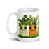 The Farm Market Dust Bunnies Mug by Bindlewood Shop is a white ceramic mug decorated with adorable cartoon vegetables featuring big eyes and smiling expressions. The design includes a green radish, an orange carrot, and an ear of corn, all standing on a bed of green grass. Plus, it's both dishwasher safe and microwave safe for added convenience.