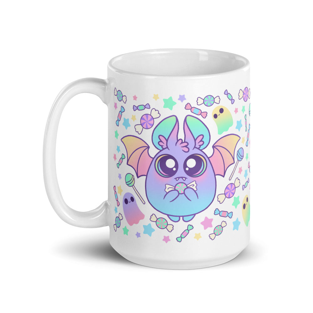 The Pastel Candy Bat Mug from Bindlewood Shop is a microwave-safe white ceramic mug. It showcases a cute, round, blue-purple bat with large eyes, small fangs, and pastel-colored wings. Surrounding the bat are colorful candies, stars, and playful ghost-like figures in a fun and whimsical design.